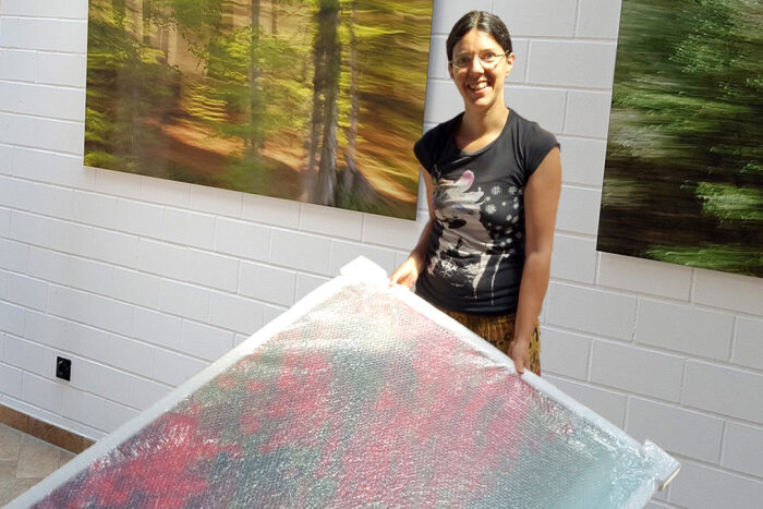 The photo artist Jennifer Scales holding a large photograph in bubble wrap. In the background, other large photographs are already on the wall