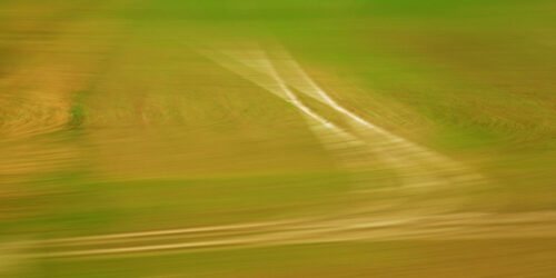 abstract photo art, a field in shades of green and brown, turned into an abstract pattern by motion blur. Two lines from a lane are a distinctive feature, they are warped by motion blur