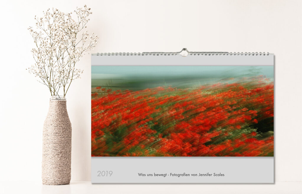 A calendar is propped up next to a vase with flowers The title page has the text: 2019 - Was uns bewegt - Fotografien von Jennifer Scales