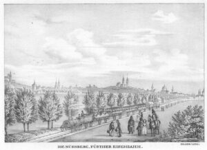 A lithograph from 1839 showing a railway line with a train and open wagons. There is a city in the background (Nuremberg), and people in the foreground.