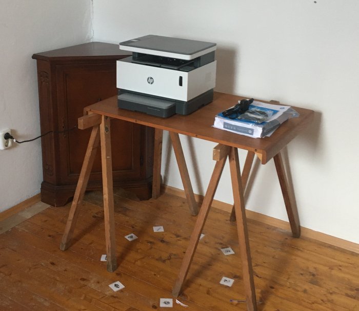 A printer stands on an improvised table. In the background, there is a corner cupboard. On the floor, there are stickers with symbols in a circle.