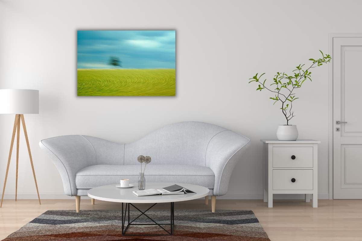 Fotografie "Sturmhimmel" von Jennifer Scales an der Wand eines modern eingerichteten Wohnzimmers. Ein gelblich-grünes Feld in dem sich durch Bewegungseffekte Halbkreise abzeichen, ein verwischter Baum am Horizont und ein dunkelblauer Himmel mit Regenwolken
