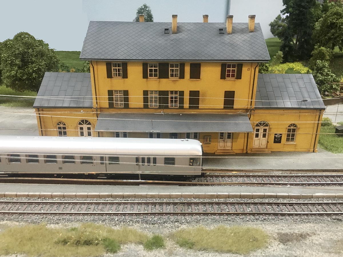 Nachbau des Bahnhofs Peißenberg in einer Modelleisenbahnlandschaft. Im Vordergrund ist ein Zug auf den Gleisen zu sehen.