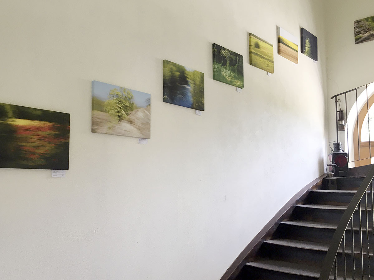 Eine Kunstausstellung: kleinformatige Fotografien hängen entlang einer Treppe ins Obergeschoss.