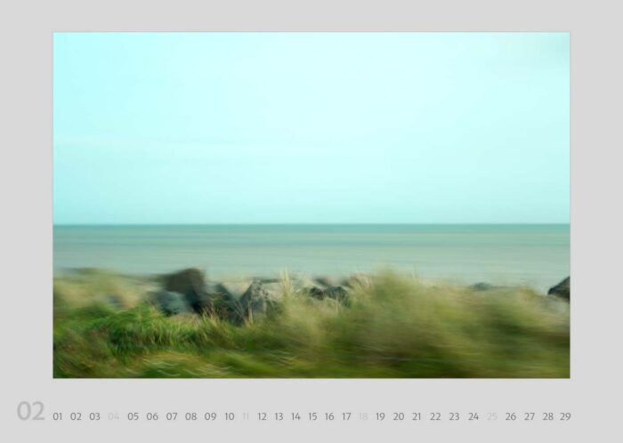 Kalenderblatt 02 aus dem Kalender "Travelscapes 2024" von Jennifer Scales. Das Motiv ist eine dynamische Fotografie mit Bewegungseffekten von einem Küstenstreifen. Im Vordergrund sind Steine und Gras zu erkennen, das Meer im Hintergrund ist durch die Bewegung zu einer geometrischen Textur verfremdet