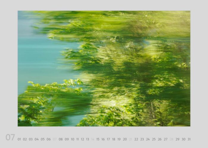 Calendar page 07 from the calendar "Travelscapes 2024" by Jennifer Scales. The motif is a dynamic photograph with motion effects of a treetop in front of a turquoise alpine lake