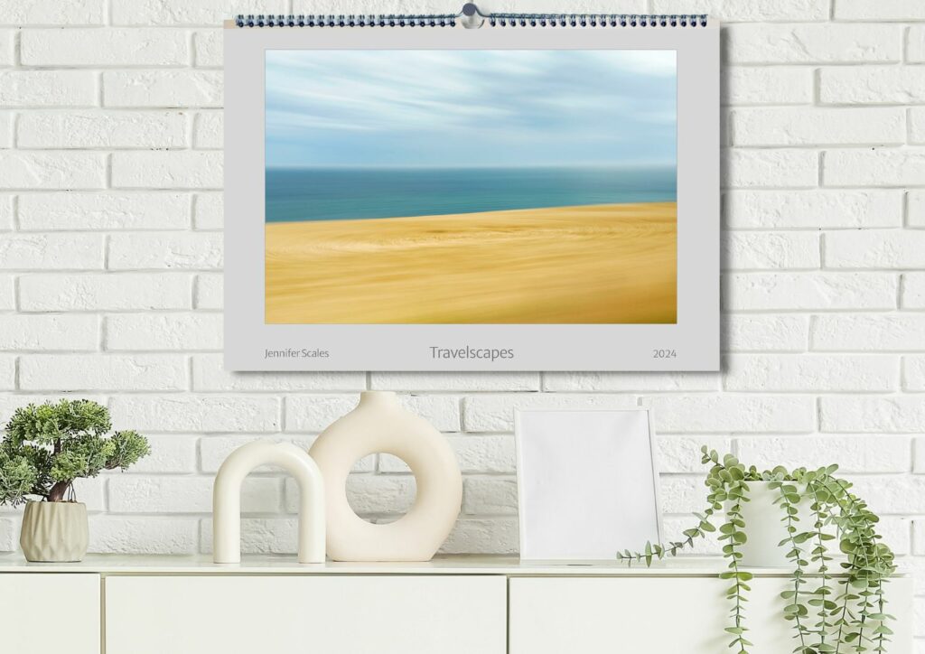 Der Foto-Kunst Kalender 2024 von Jennifer Scales mit dem Titel "Travelscapes" hängt an der Wand über einem Sideboard